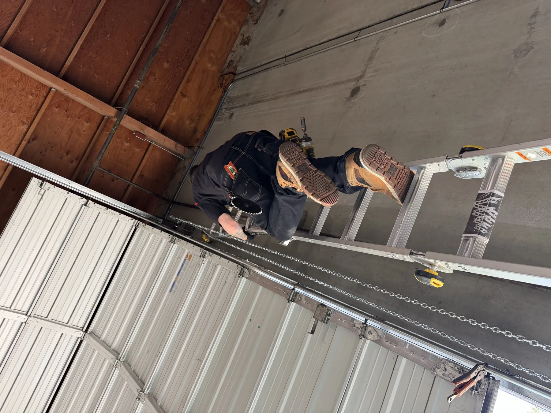 Valiant technician on a ladder servicing a commercial overhead door chain system