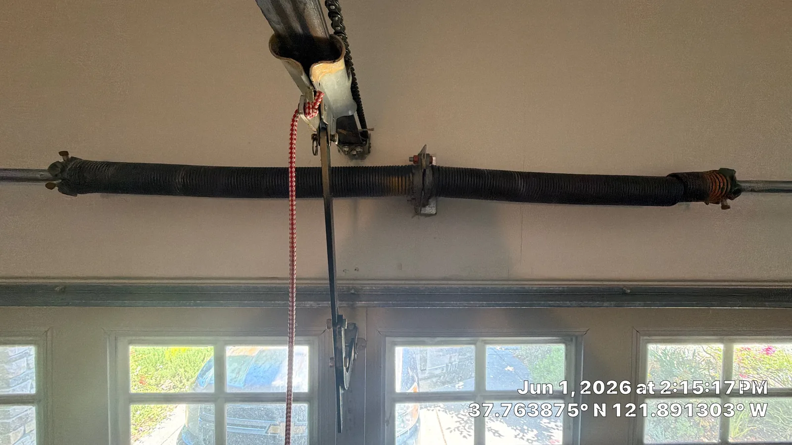 Worn and broken torsion springs above a closed garage door.