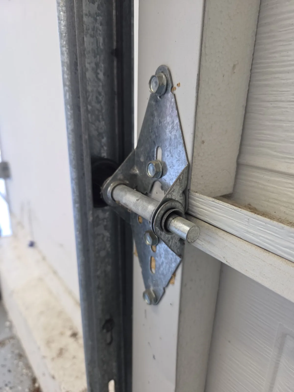 Chewed, worn garage door roller at the hinge and vertical track.