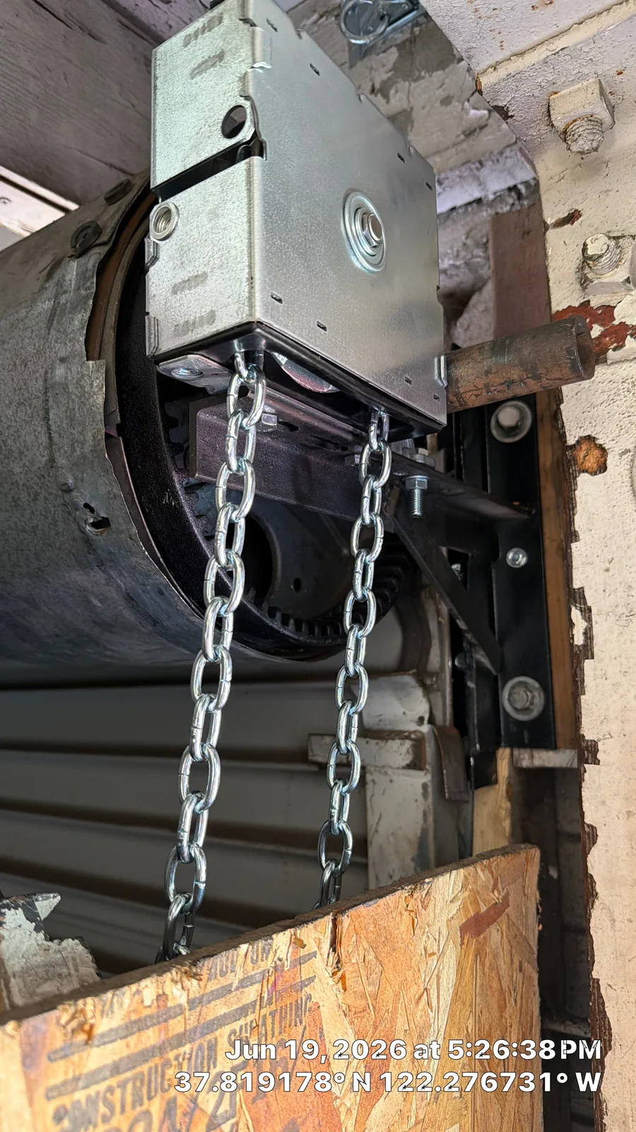 Completed commercial garage door chain-reduction hoist and supported drive hardware.