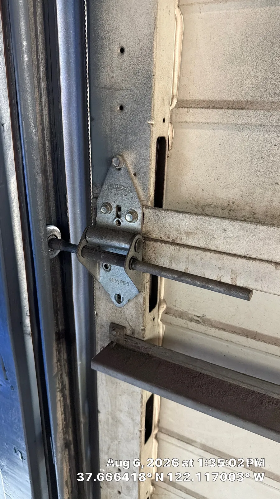 Worn garage door roller and loose hinge hardware beside the vertical track.