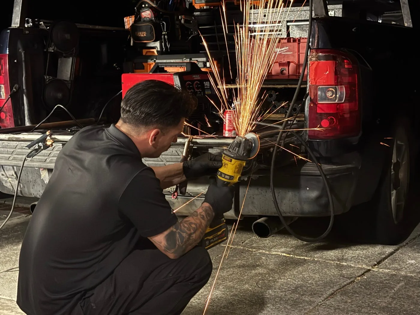 Valiant Garage Door technician using an angle grinder on a steel bar at his work truck at night, throwing sparks during custom metal fabrication