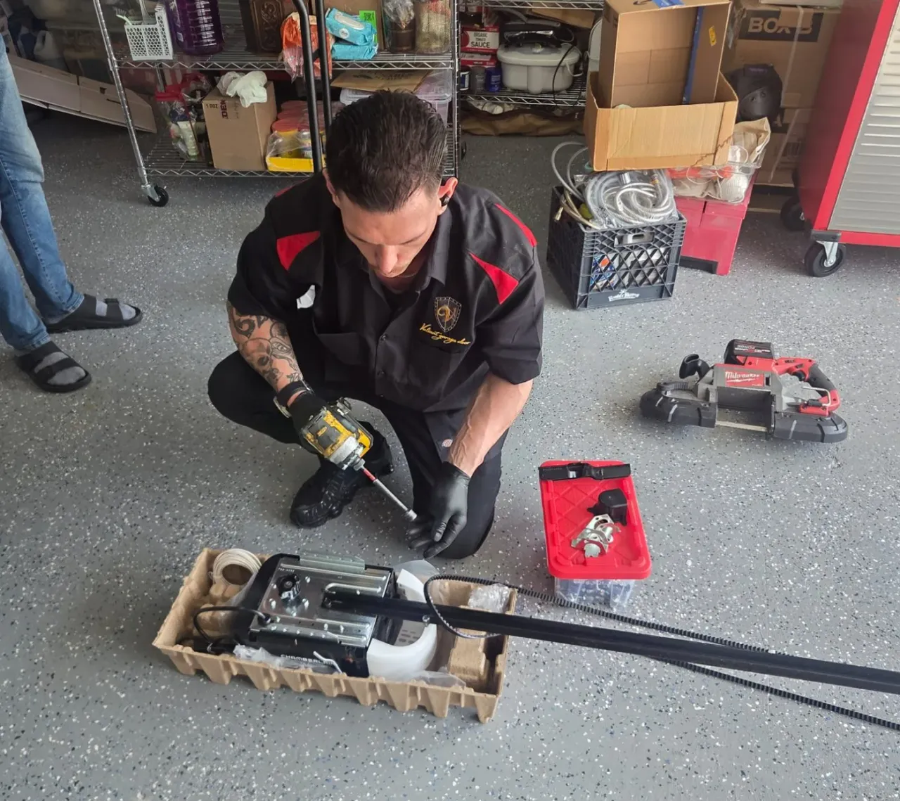 Valiant Garage Door technician in a branded work shirt installing a new Chamberlain belt-drive garage door opener on a Pleasanton garage floor