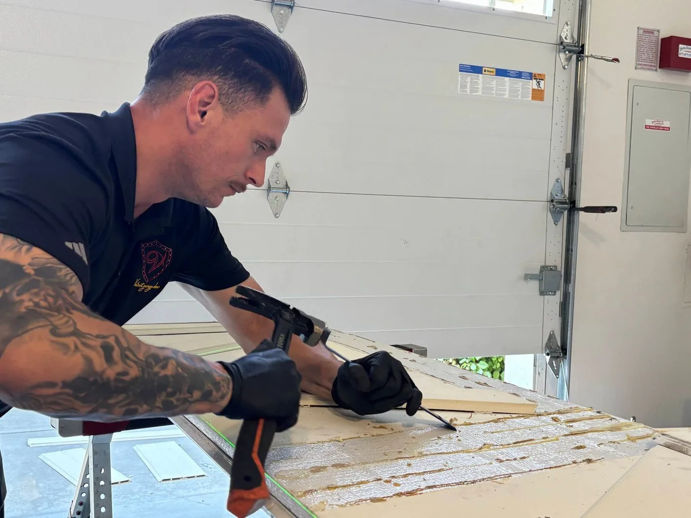 Valiant Garage Door technician clamping and repairing a garage door panel beside a freshly installed white sectional door in Pleasanton